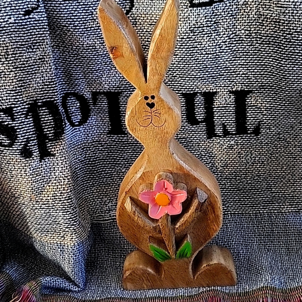 Little Easter Bunny carved out of wood with holding a pink flower in his hands